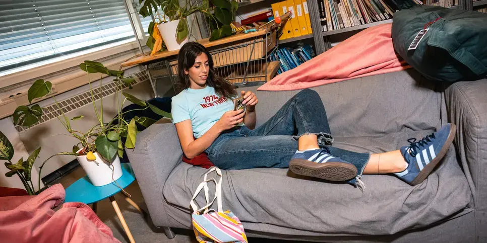 Student op bank in studentenkamer met telefoon in hand